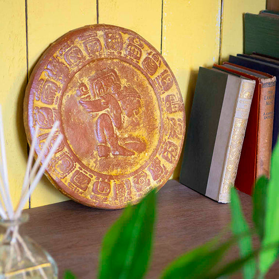 A ceramic Mayan Calendar displayed on a bookshelf